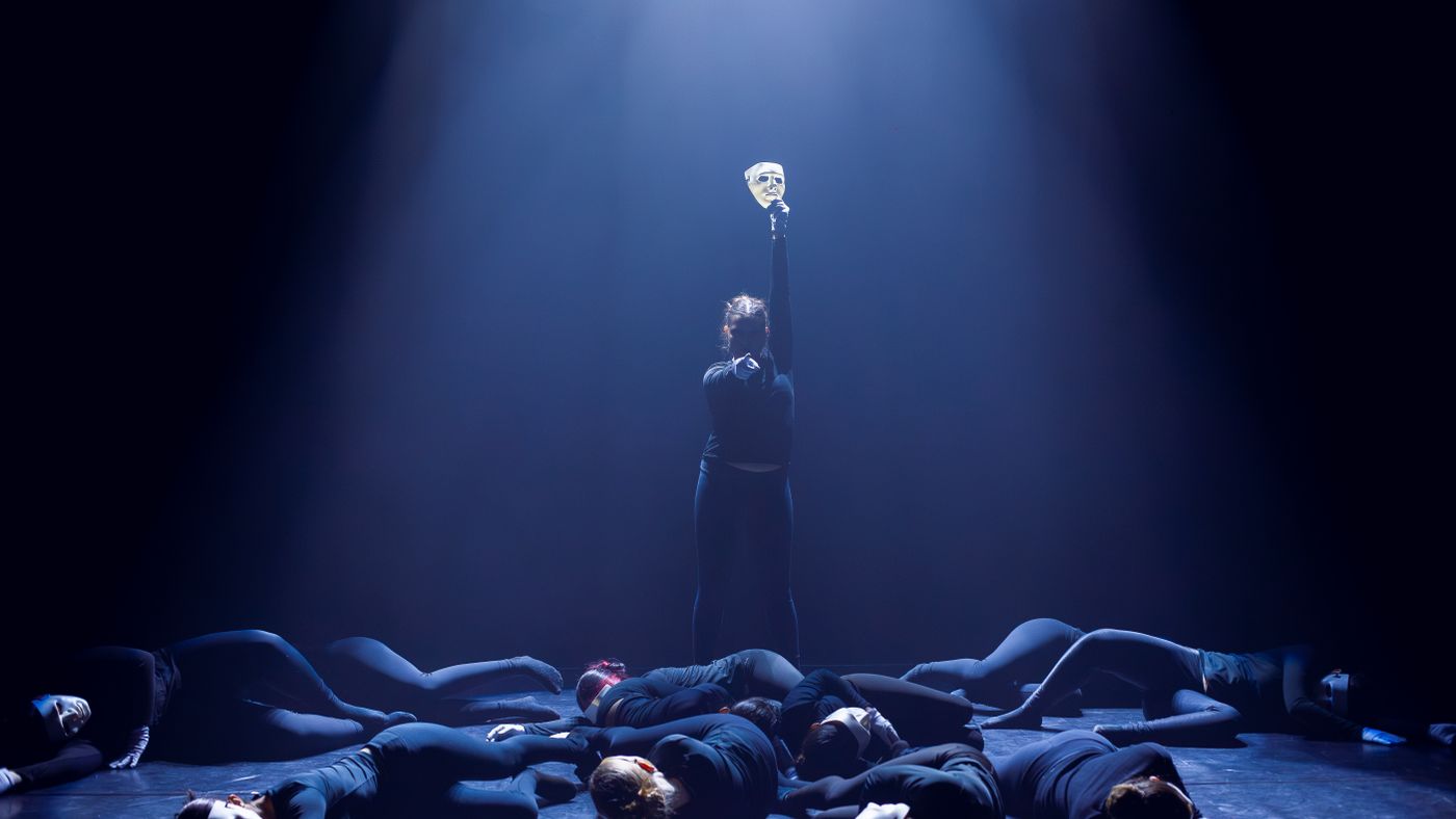 Captivating dance performance on stage with dramatic lighting and masks.